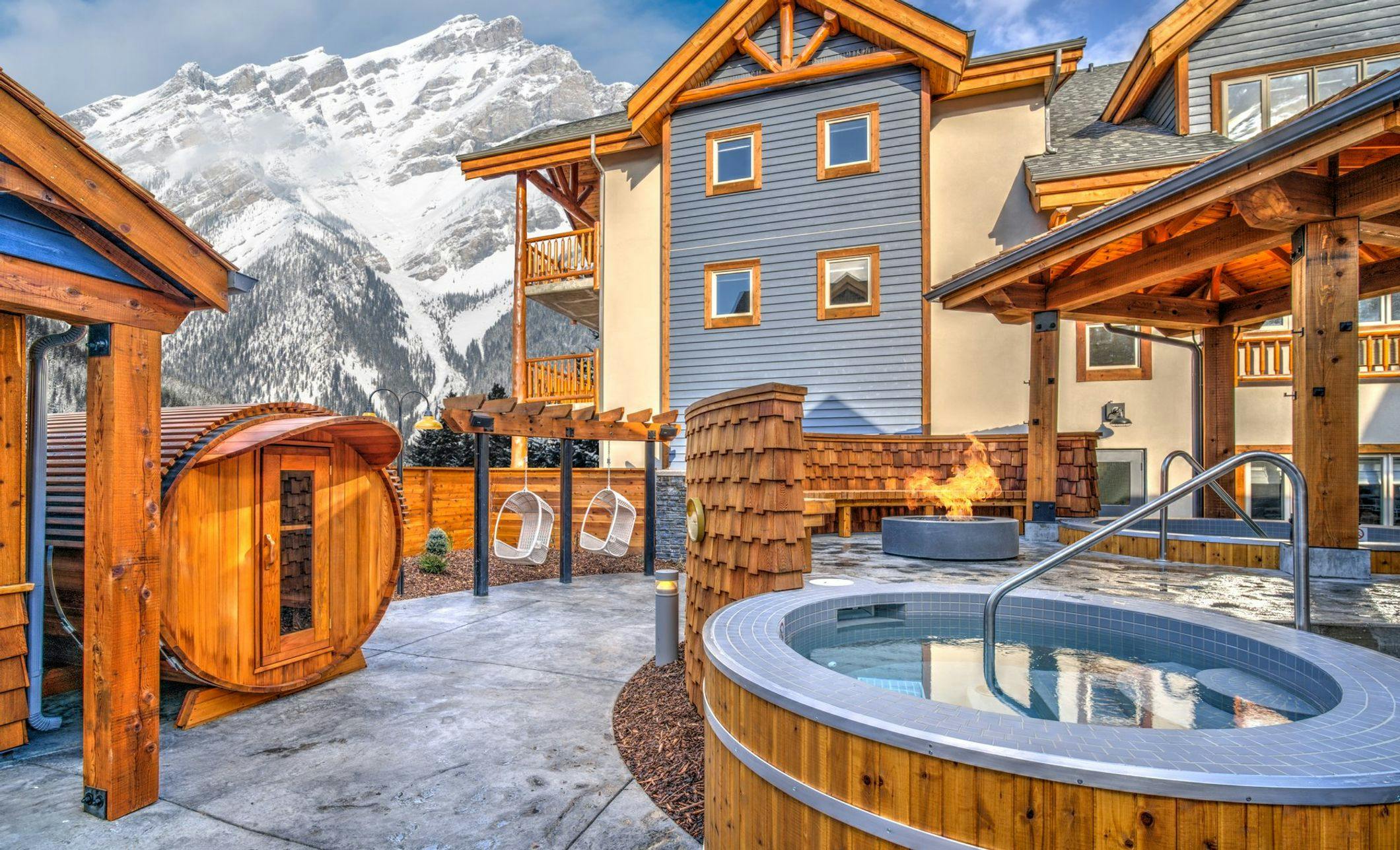Outdoor amenities at a hotel including a hot tub, fire pit, and seating. Snow covered mountain in the background