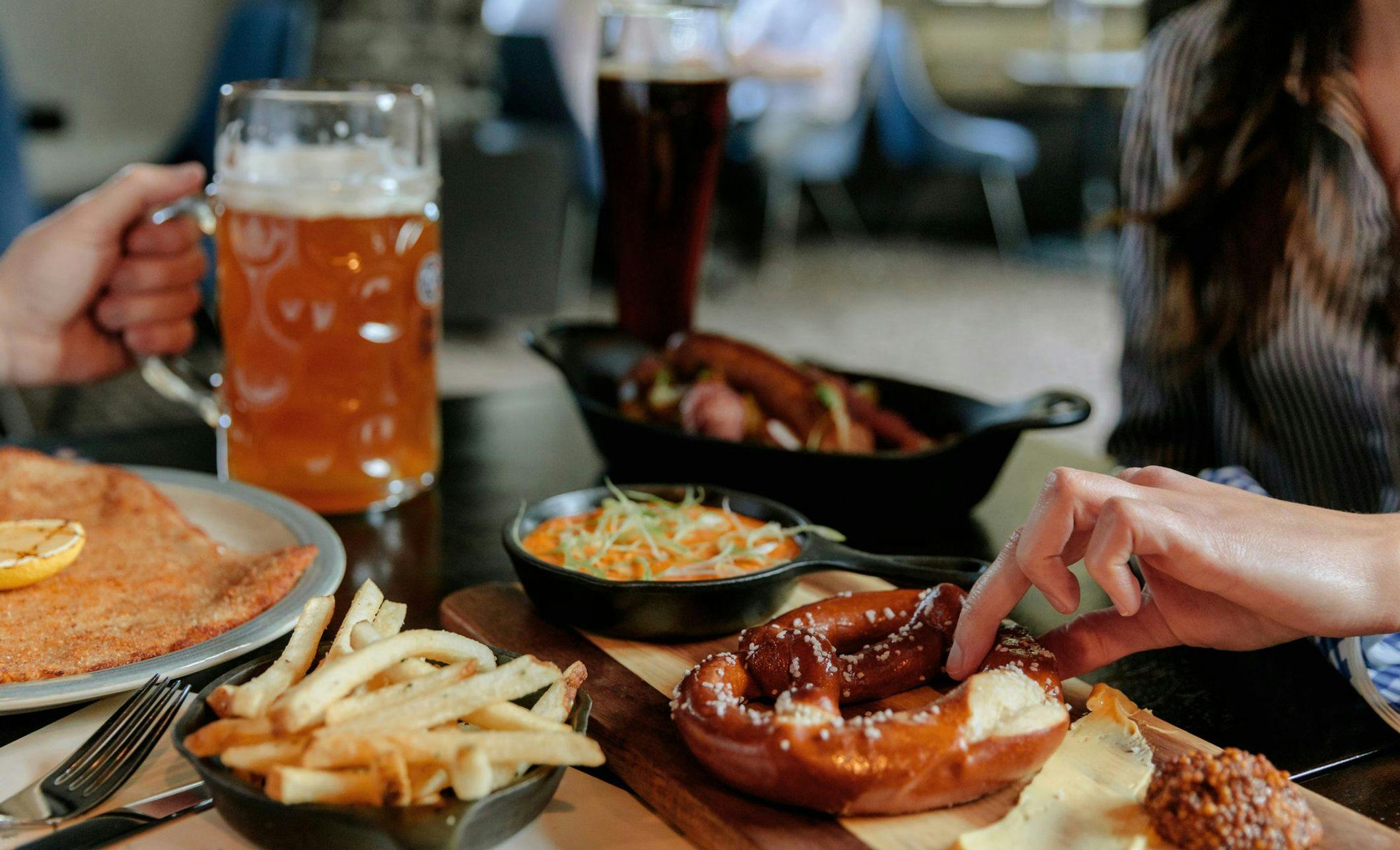 A table features beer and plated food including warm pretzels, fries, and appetizers