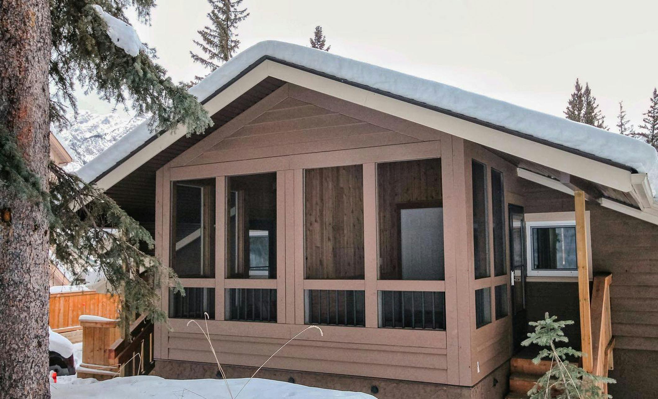 Cabin-style accommodation with a covered front porch, surrounded by snow