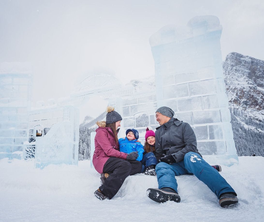 A family of four wearing all their snow gear sitting in front of a giant ice castle