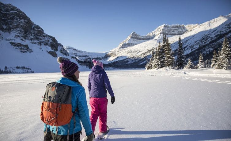 Two people snowshoeing along a frozen lake on a sunny winter day