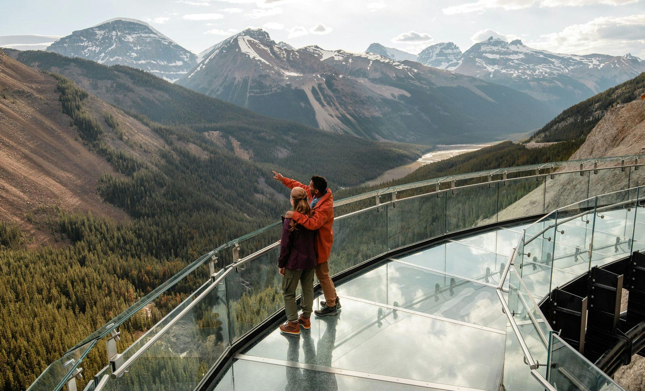 Couple standing on a glass skywalk overlooking mountains