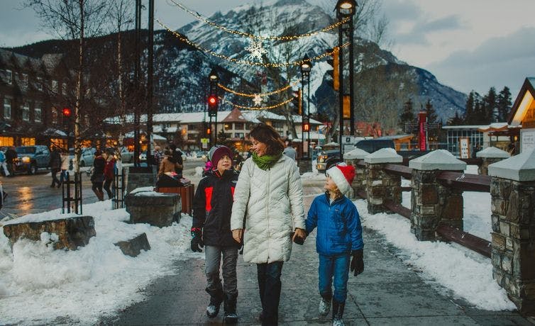 A family walking down Banff Avenue with Christmas lights and mountains behind them