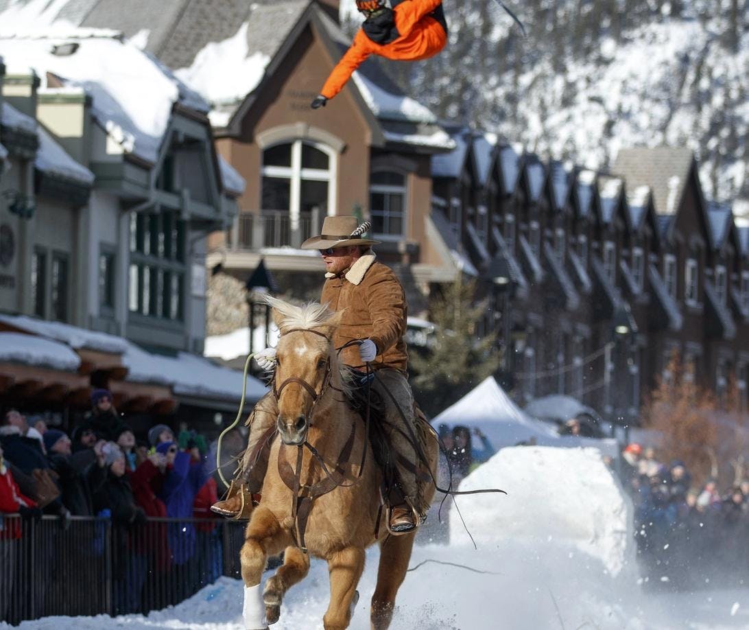 Skijoring: A person riding a horse pulls a skiier behind him performing tricks and jumps