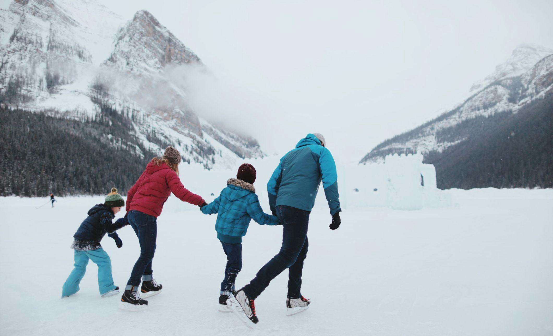 A family of four holding hands and skating towards an ice castle on the frozen Lake Louise 