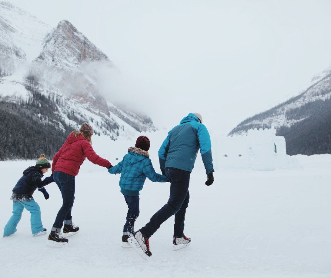 Family of four skating on a frozen lake with mountains in the background