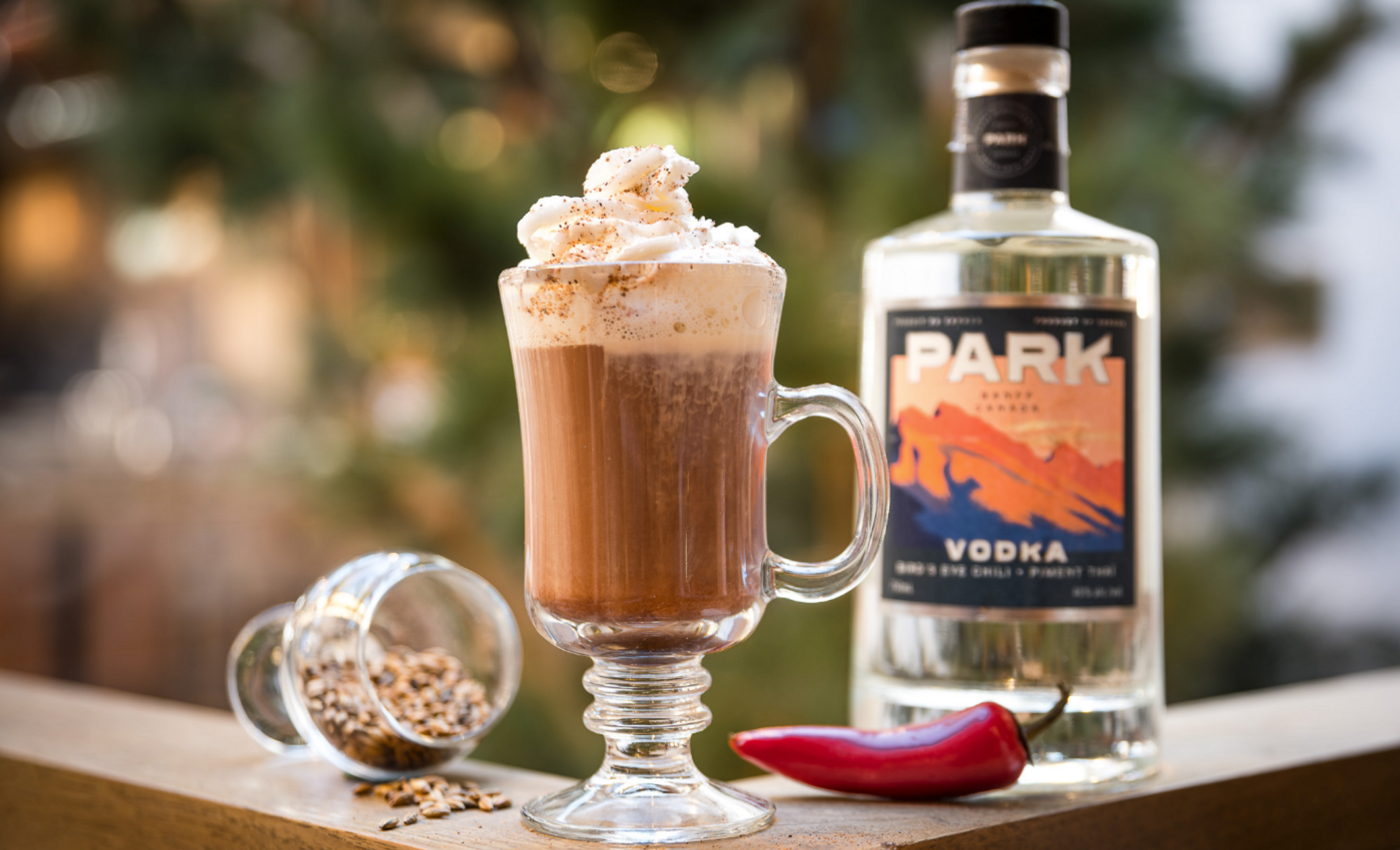 A hot chocolate beside a liquor bottle with a Christmas tree in the background.