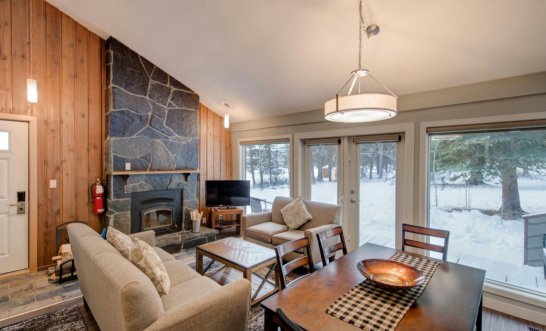 Cabin with stone fireplace, couches, and dining room table - snow outside