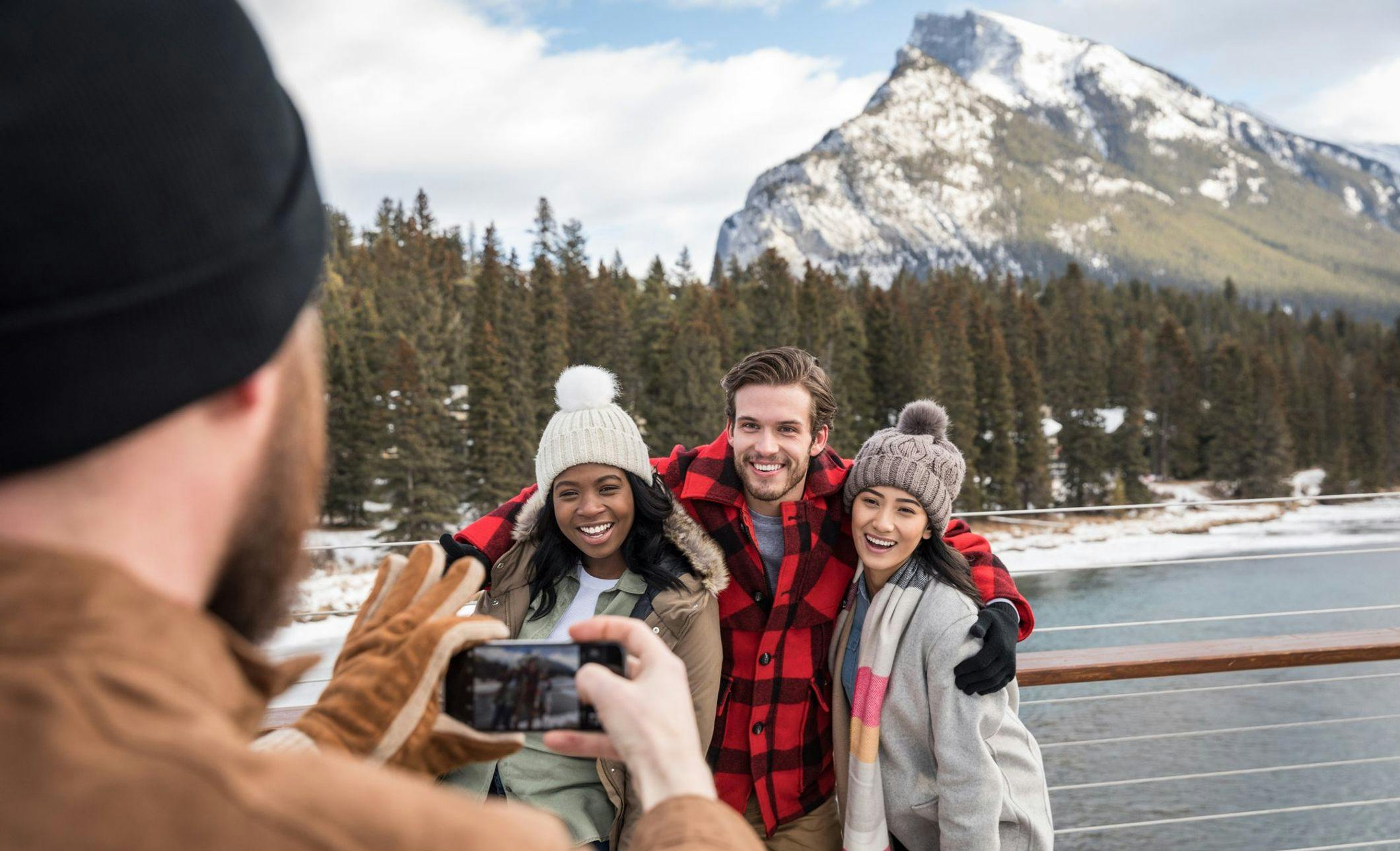 Three friends pose for a photo wearing light winter layers and a snowy Mount Rundle behind them