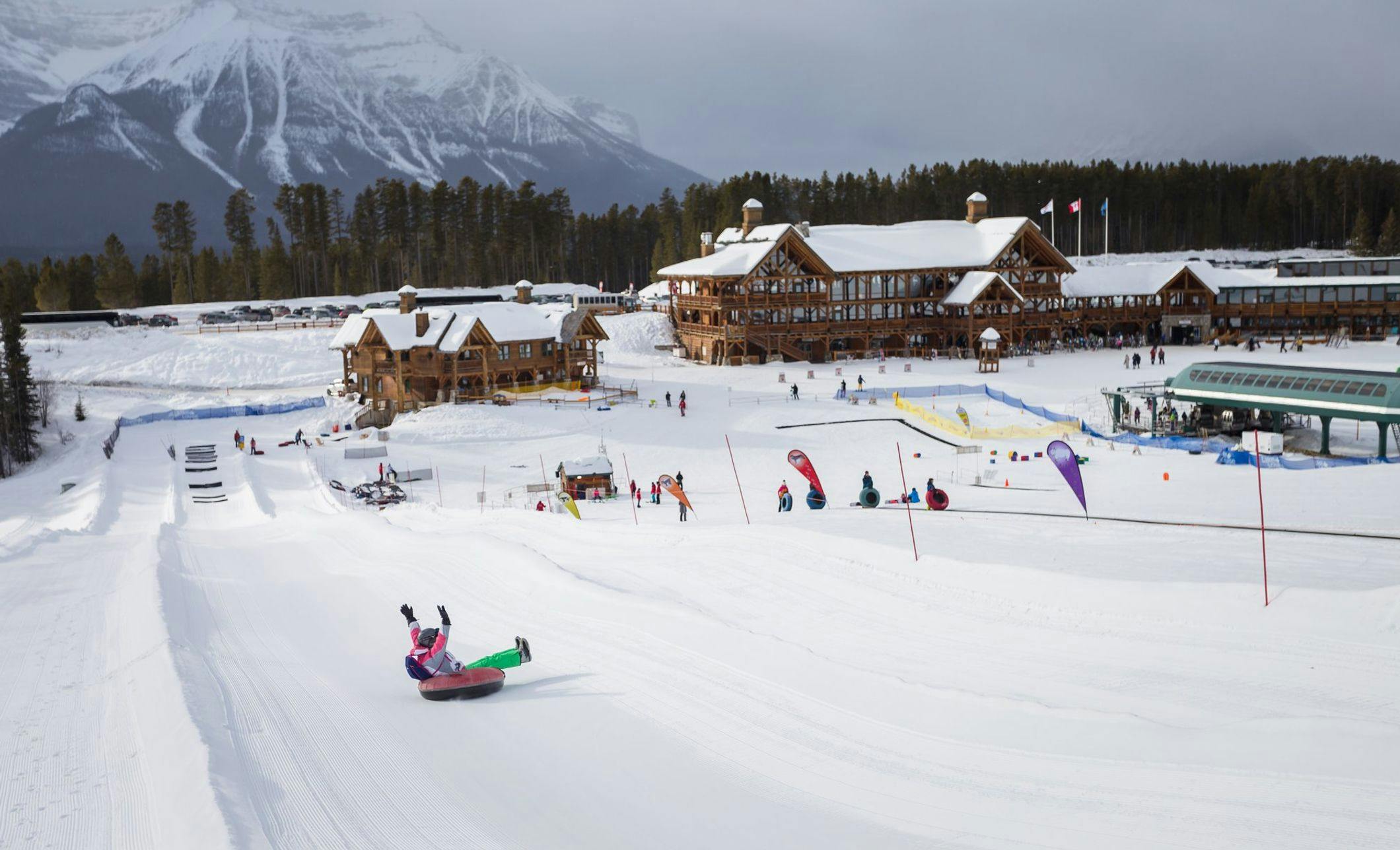 A child tubing down a long run with the Lake Louise Ski Resort chalets in the background