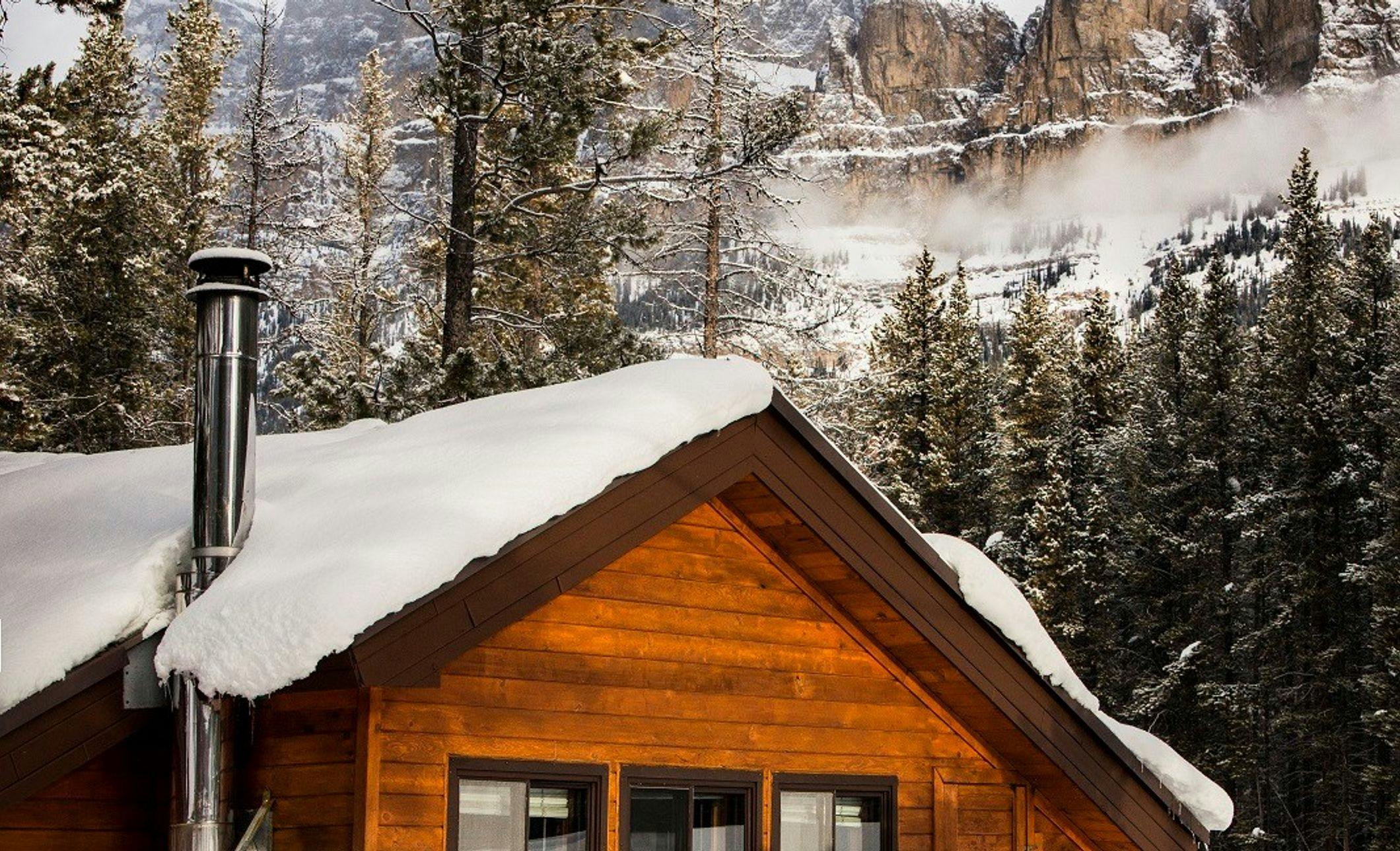 A snow-covered wooden chalet with towering mountains in the background