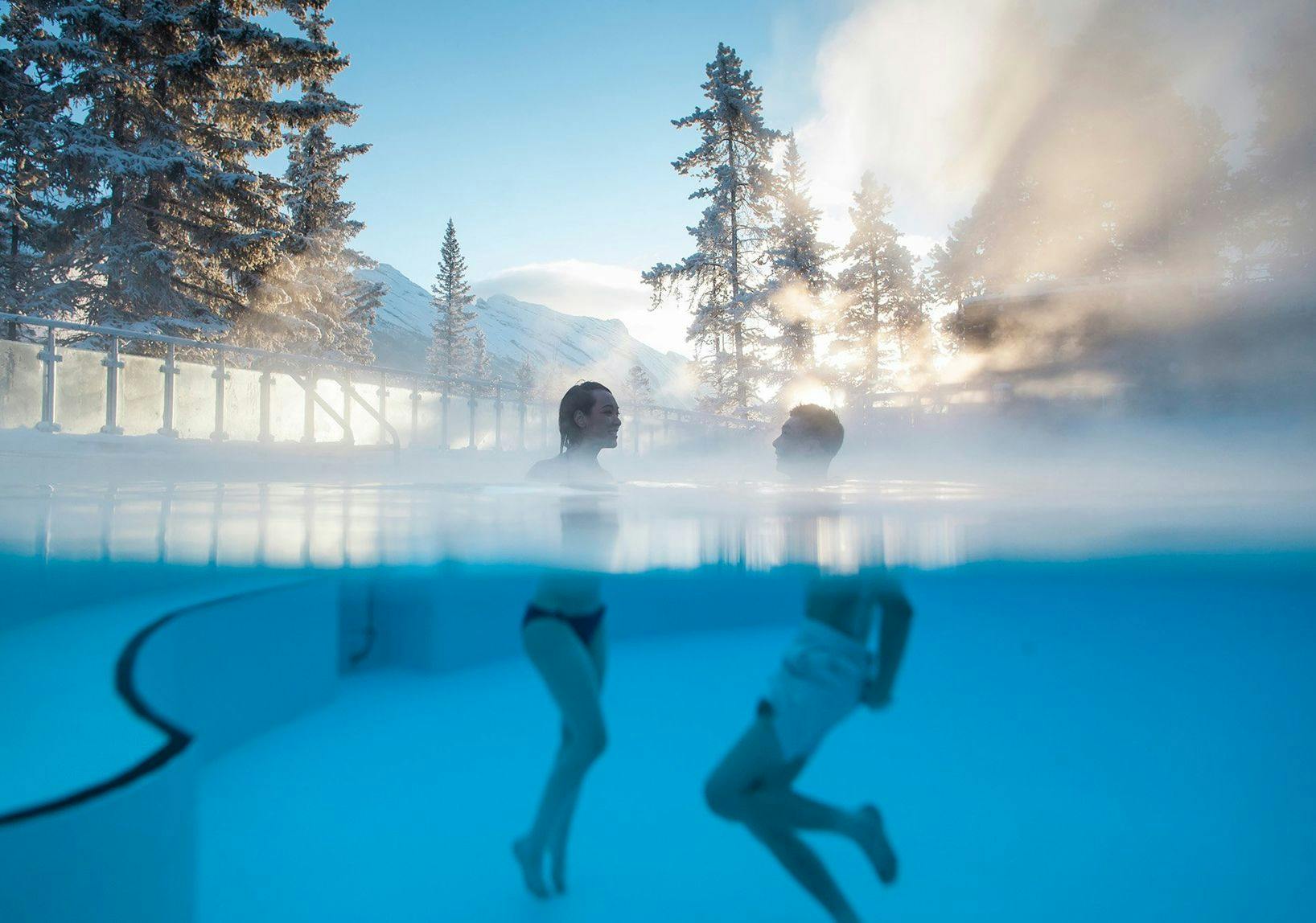Two people in the Banff Upper Hot Springs in Banff National Park with sunlight pouring through the trees behind them.