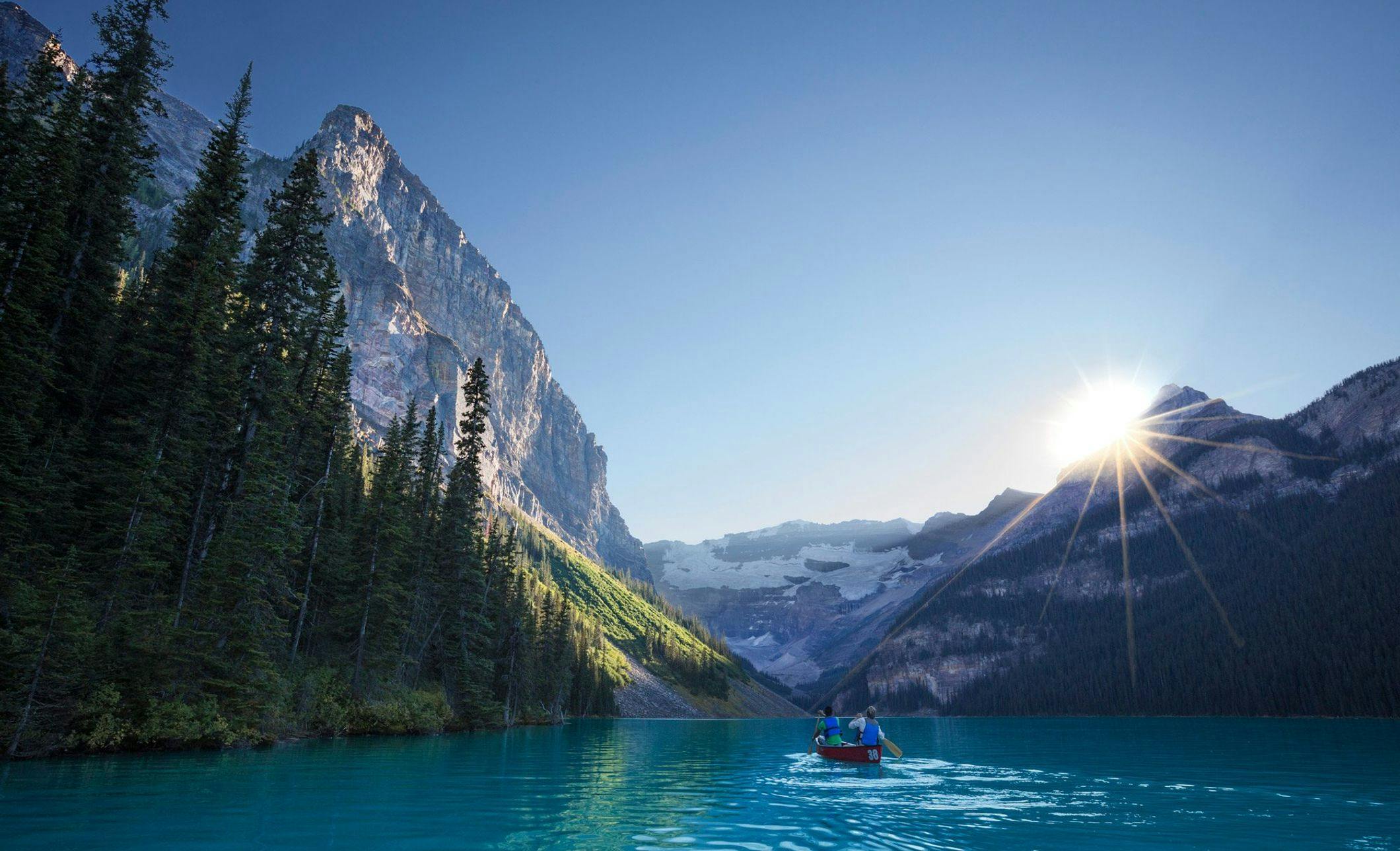 The sun peaks out from behind Mt. Victoria as paddlers navigate their canoe over the emerald waters of Lake Louise