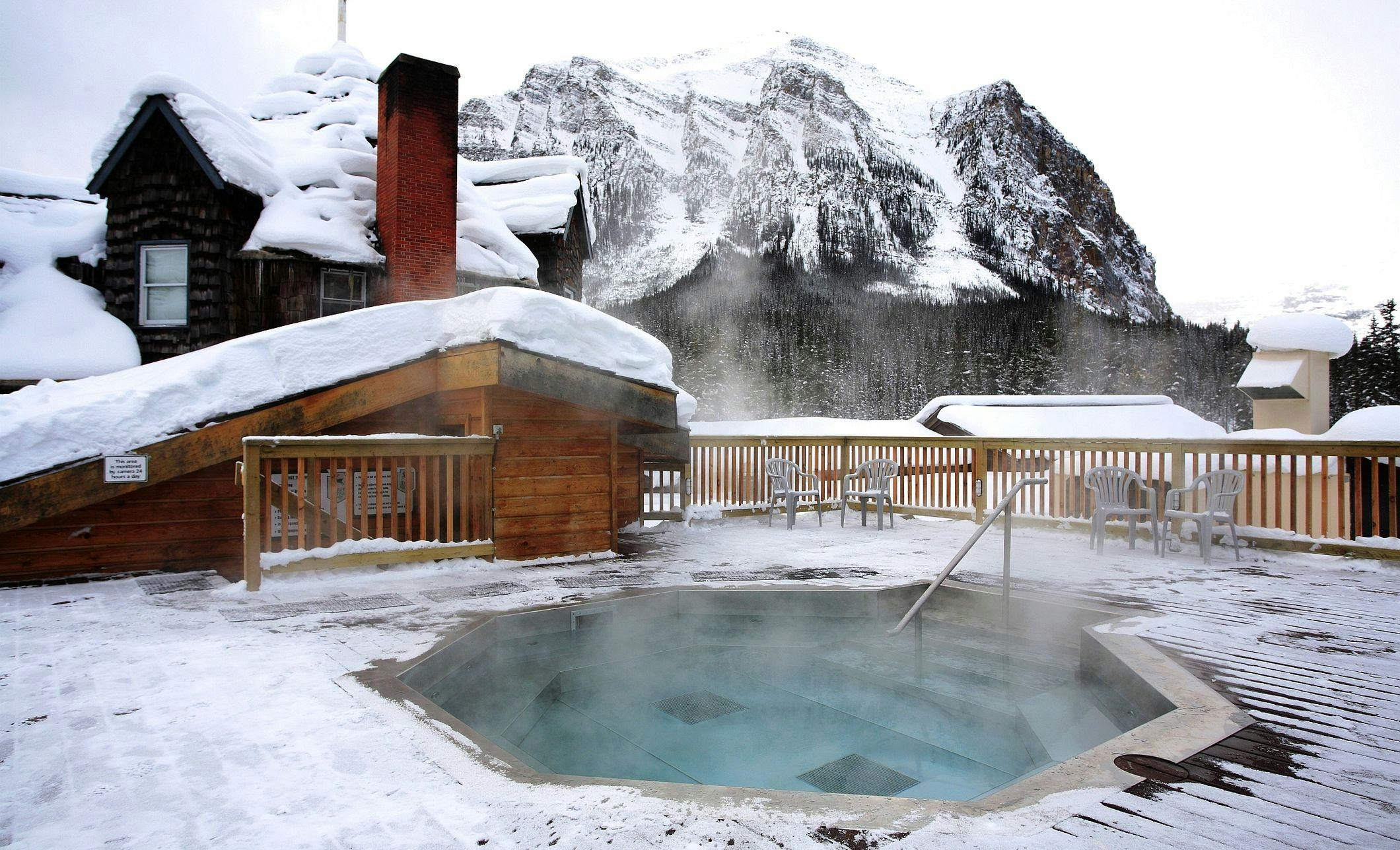 A rooftop hot tub in the winter with snow on the ground and snow-capped mountains
