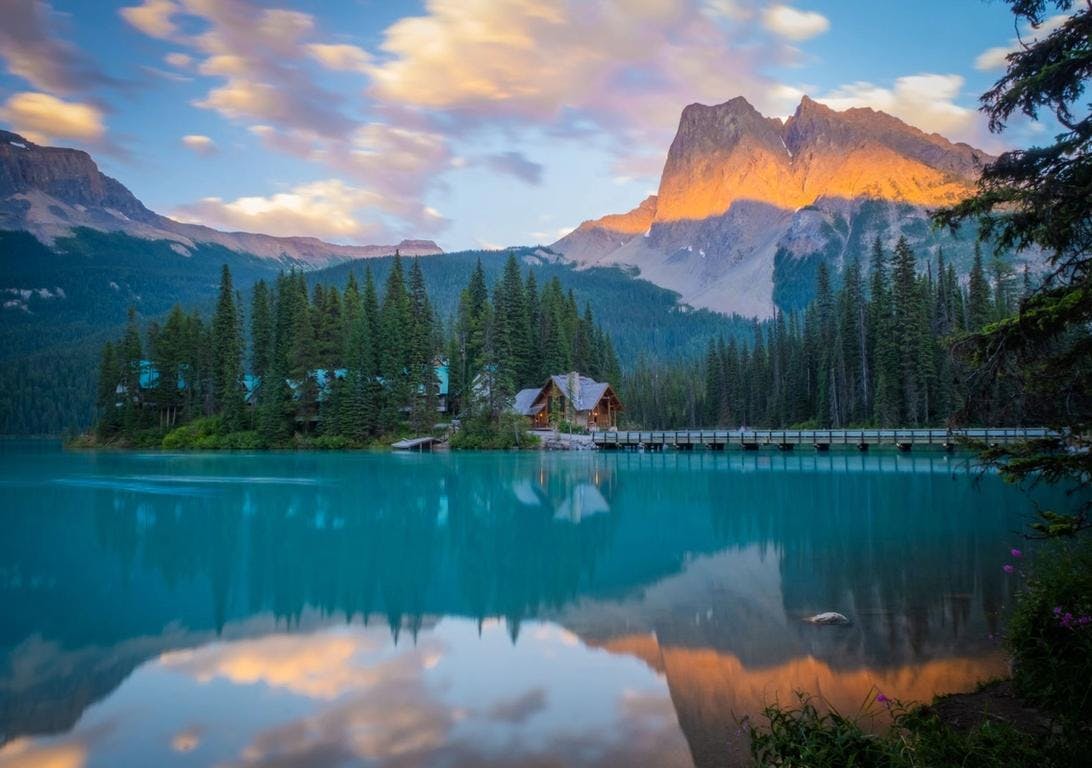 The Emerald Lake Lodge sits on an island at Emerald Lake at sunset with orange light on the mountains in Yoho National Park.