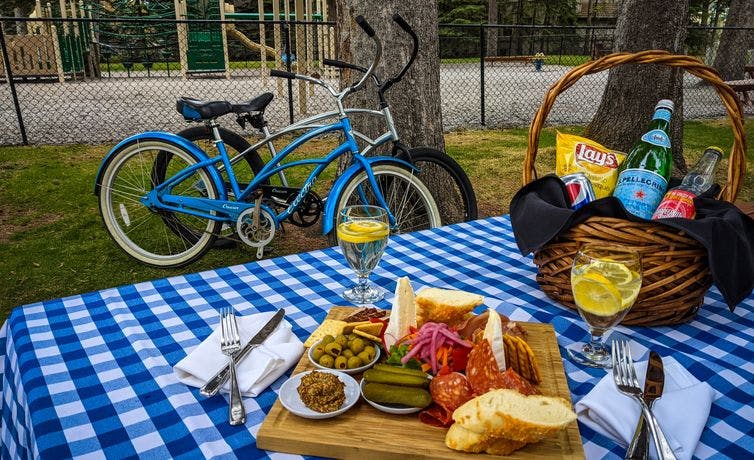 A picnic spread including a charcuterie board and sparkling water on a blue checkered blanket