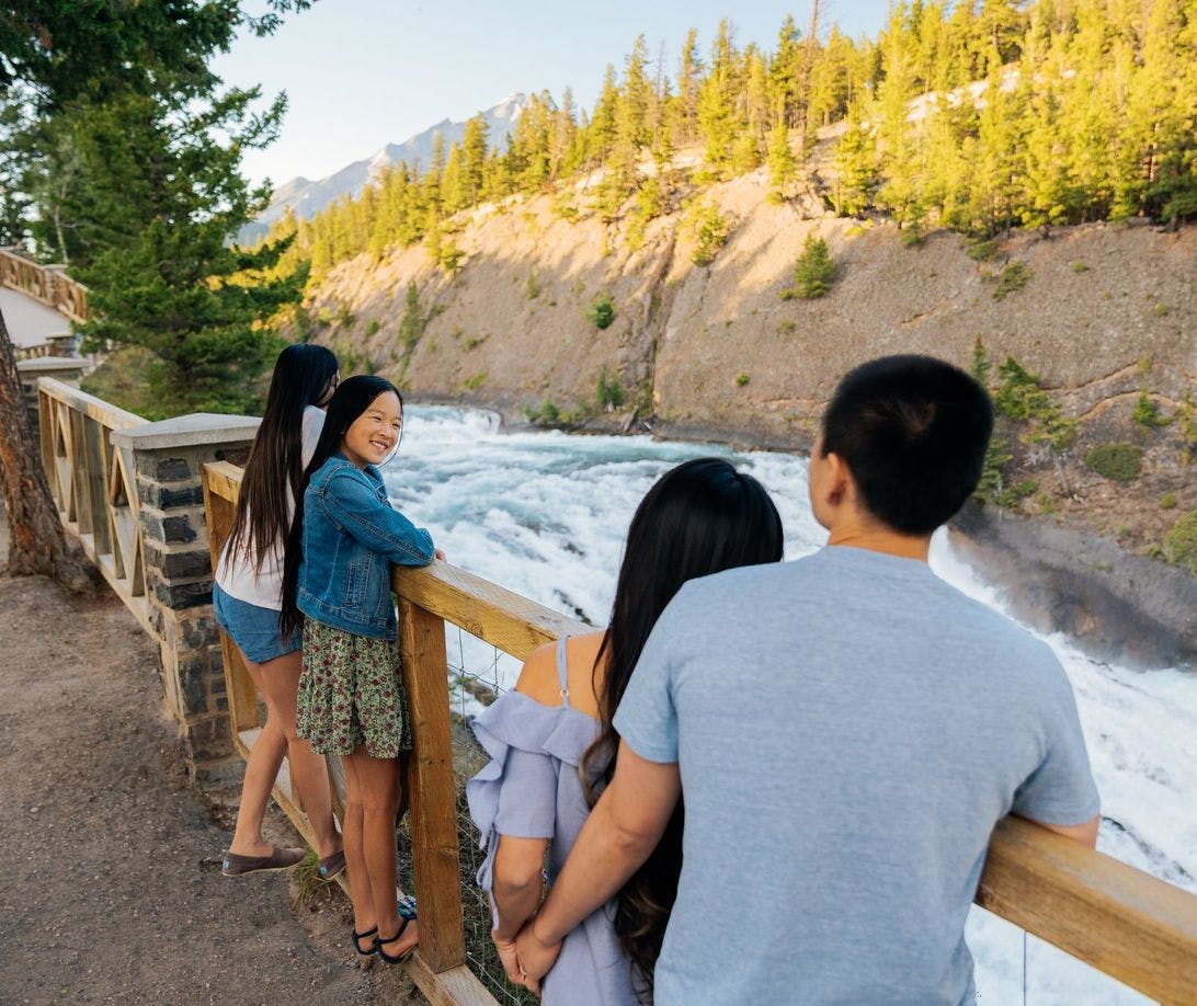 A family of four stand at a viewing platform overlooking a waterfall on a warm summer evening