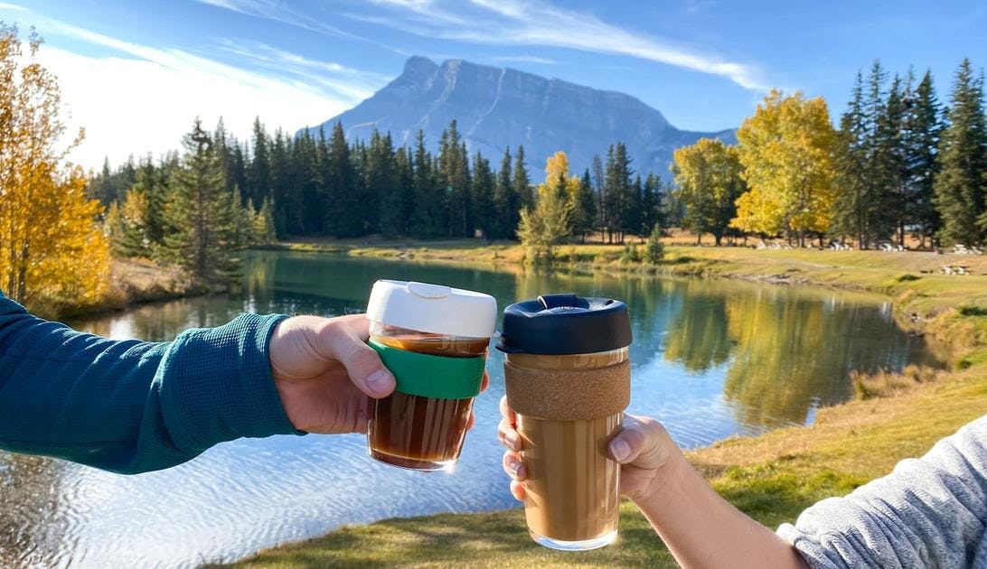 Two coffee cups "cheers-ing" at Cascade Ponds. Rundle Mountain and Fall colours in the background
