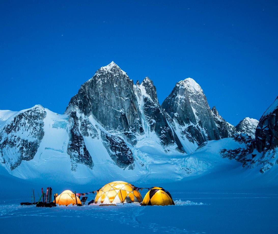 Three lit up domes on a vast snowy field with skis outside and mountains in the background