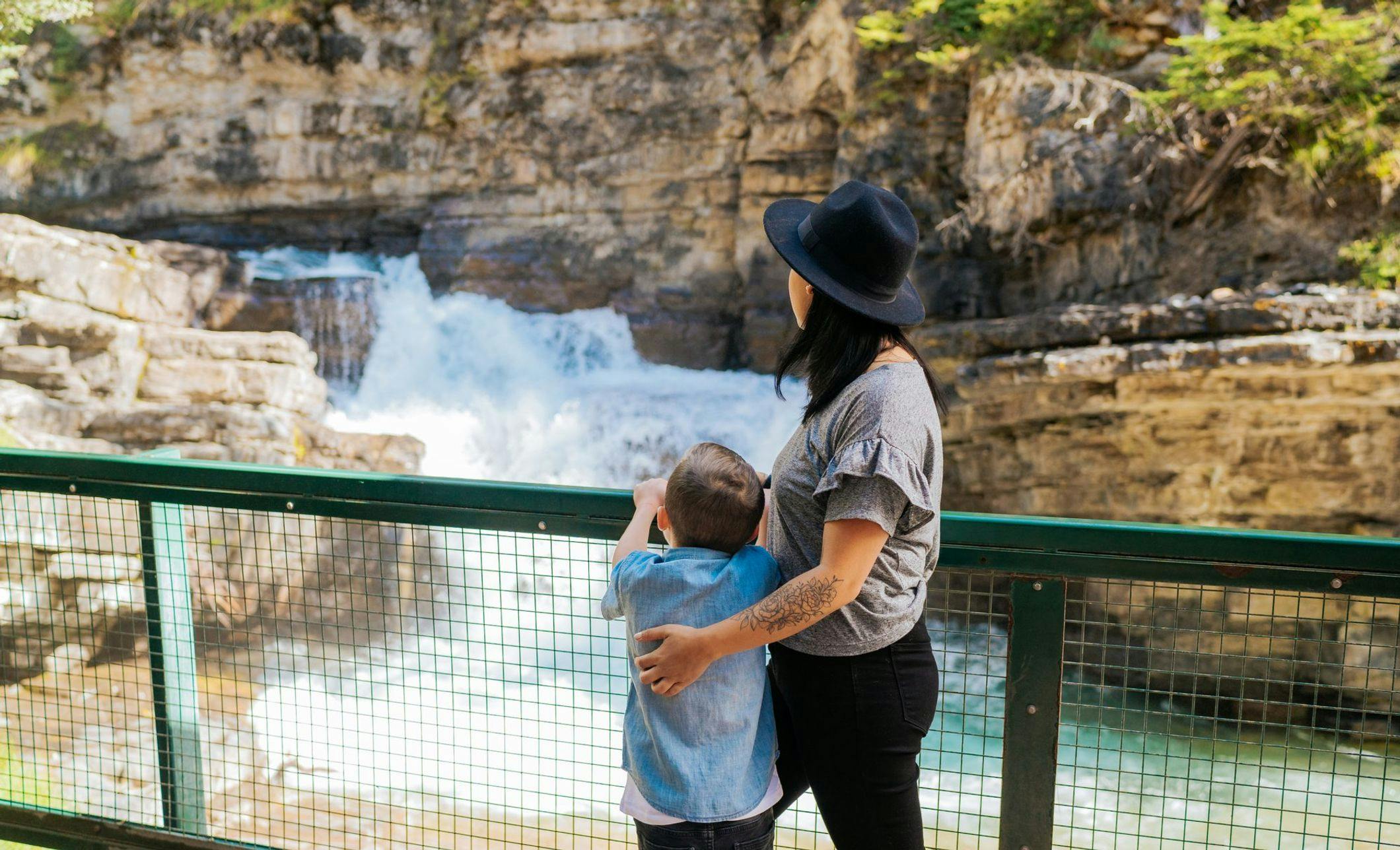 A mother and son stand alongside a railing overlooking a waterfall embedded in a large canyon