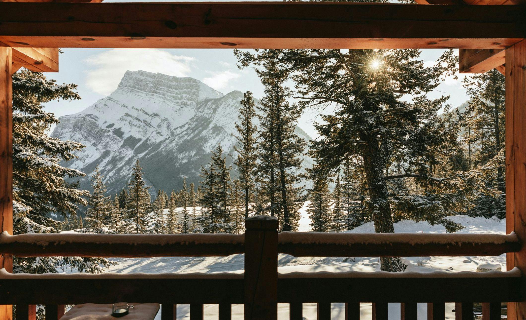 Window view of snow covered mountains from a log cabin