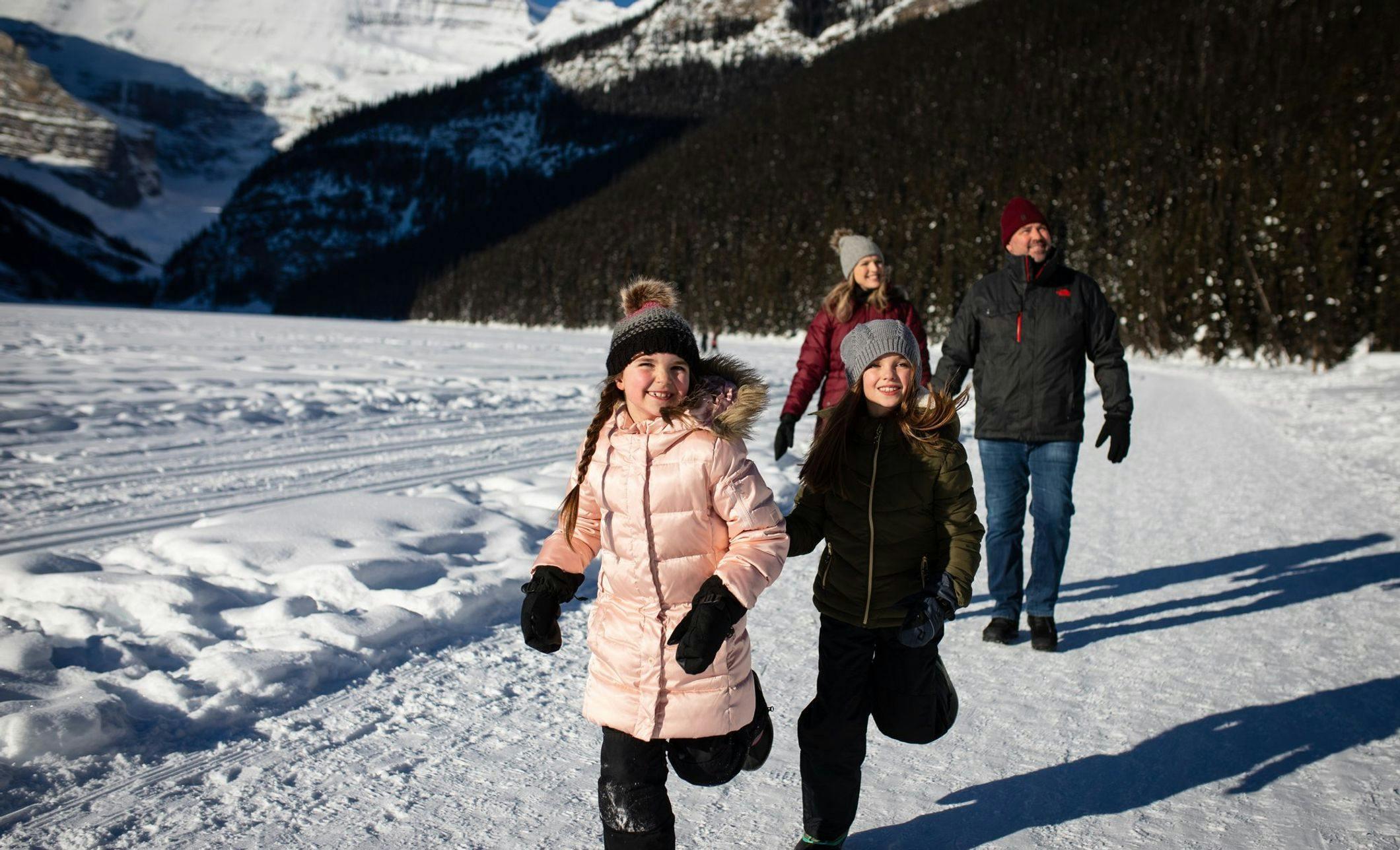 A family walks along a snow covered trail around a frozen lake