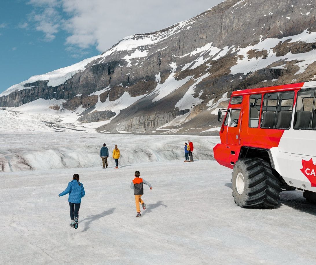 A family walks on a glacier after taking a bus pictured on the right to reach it