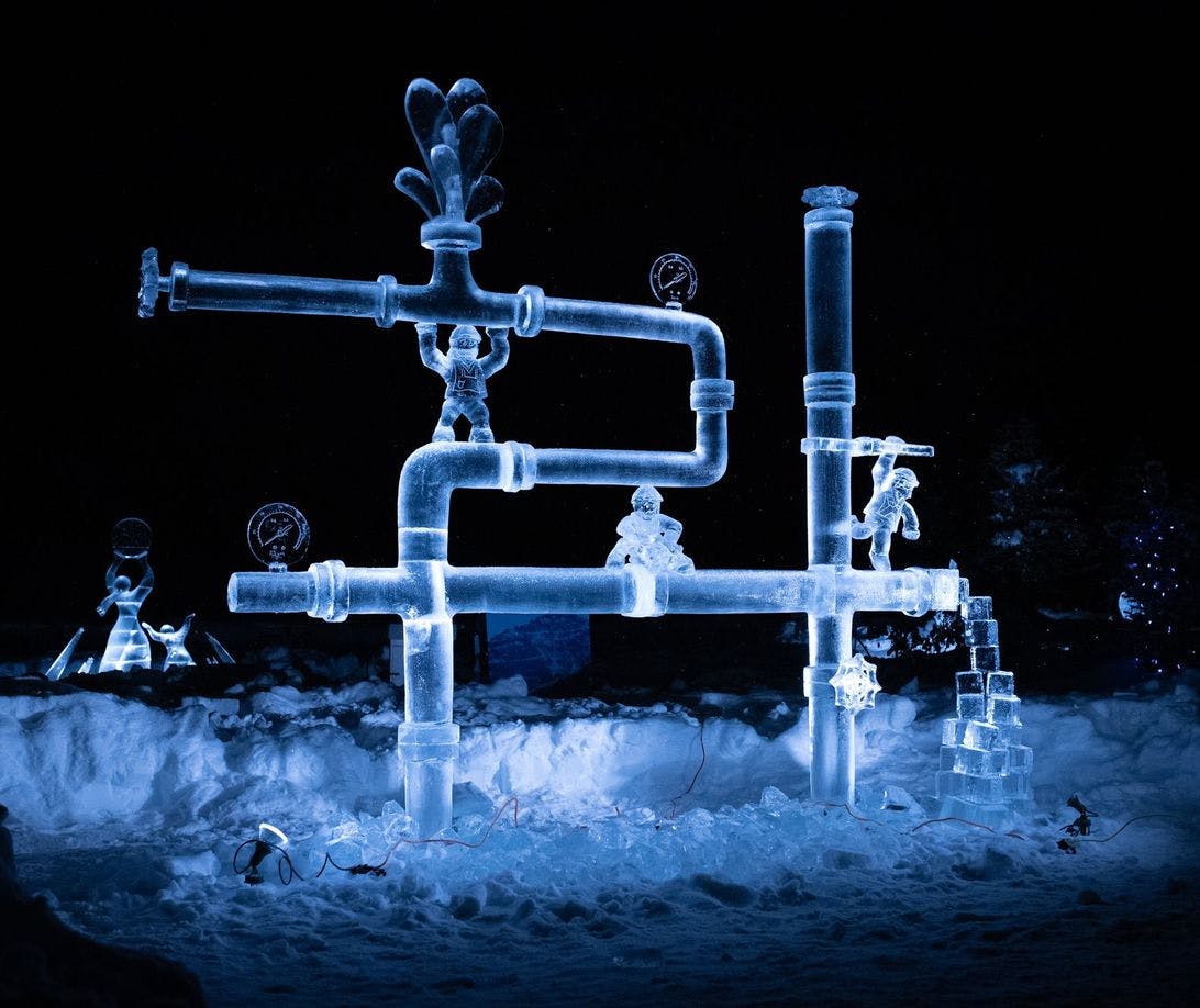 An ice sculpture of intricate pipes lit up in the evening and glowing
