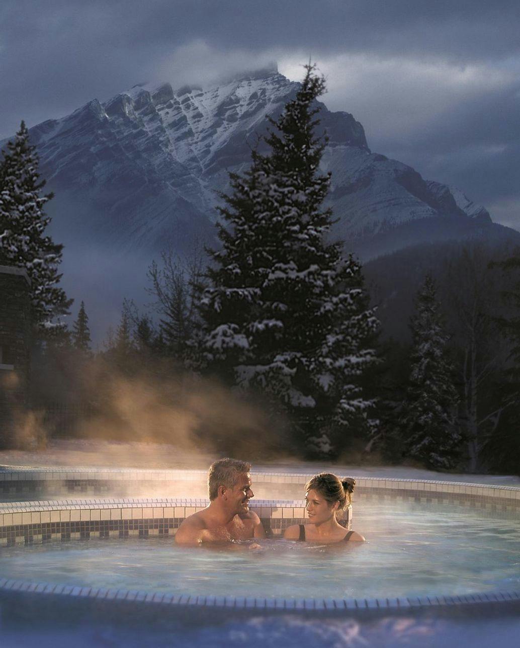 Couple in an outdoor jacuzzi in Winter with a mountain in the background