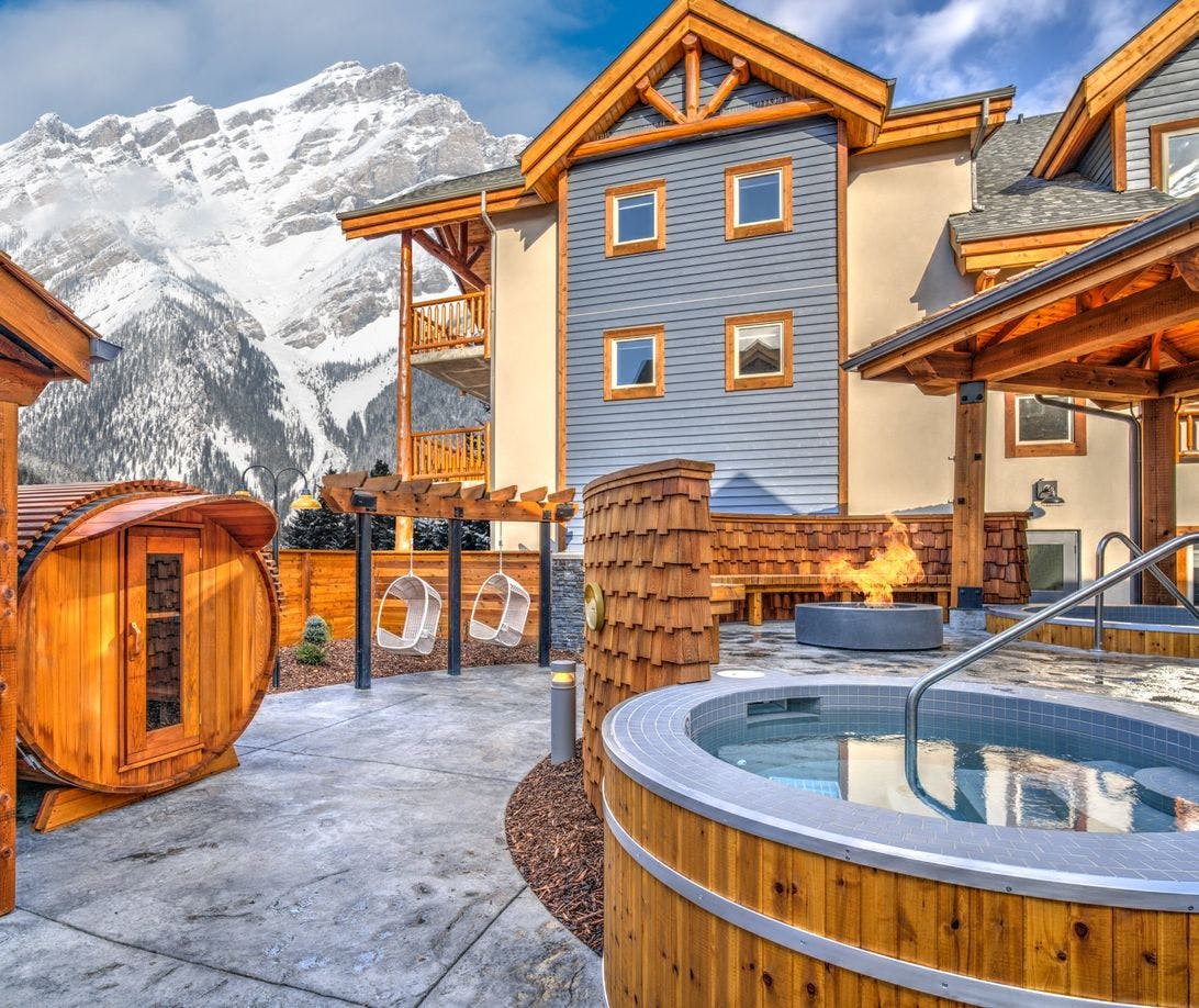 Outdoor amenities at a hotel including a hot tub, fire pit, and seating. Snow covered mountain in the background