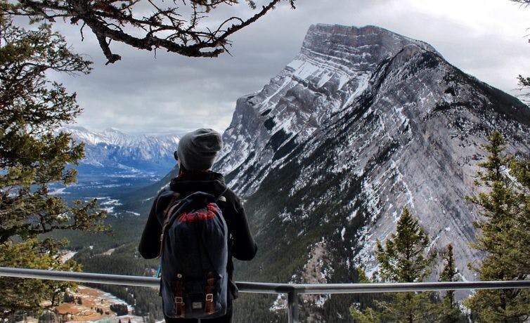 A woman stands on Tunnel Mountain looking towards Mountain Rundle surrounded by trees in Banff National Park.