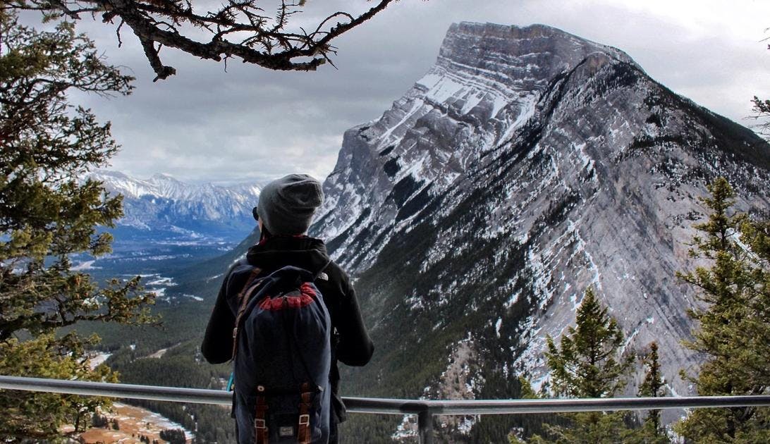 A woman stands on Tunnel Mountain looking towards Mountain Rundle surrounded by trees in Banff National Park.