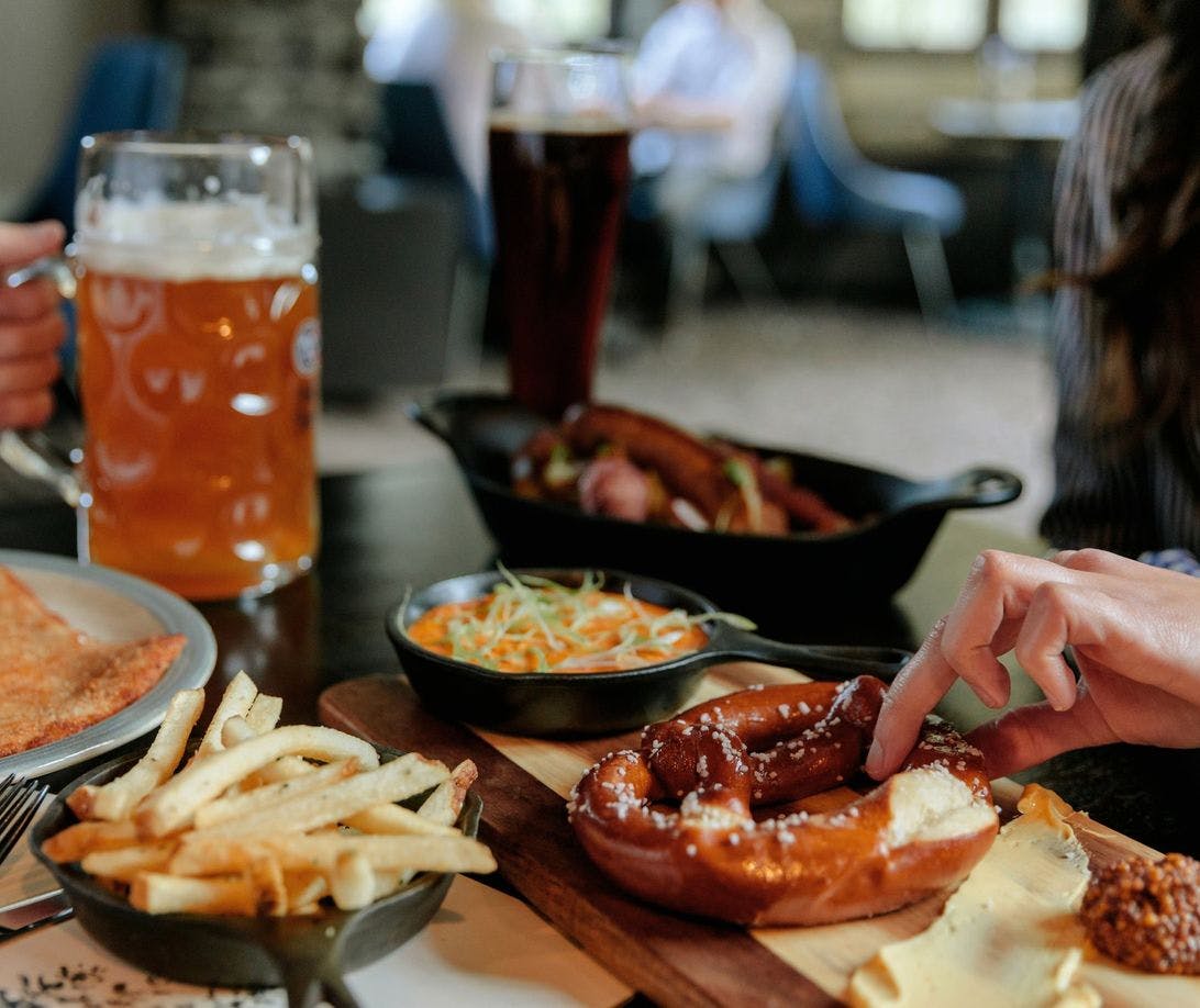 A table features beer and plated food including warm pretzels, fries, and appetizers