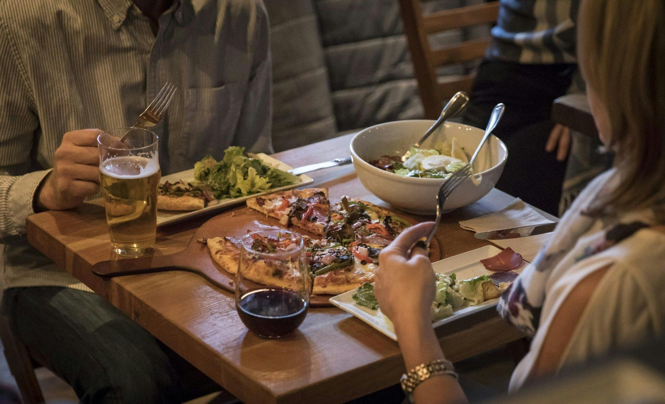 Two people enjoy sharing a meal of pizza and salad with drinks