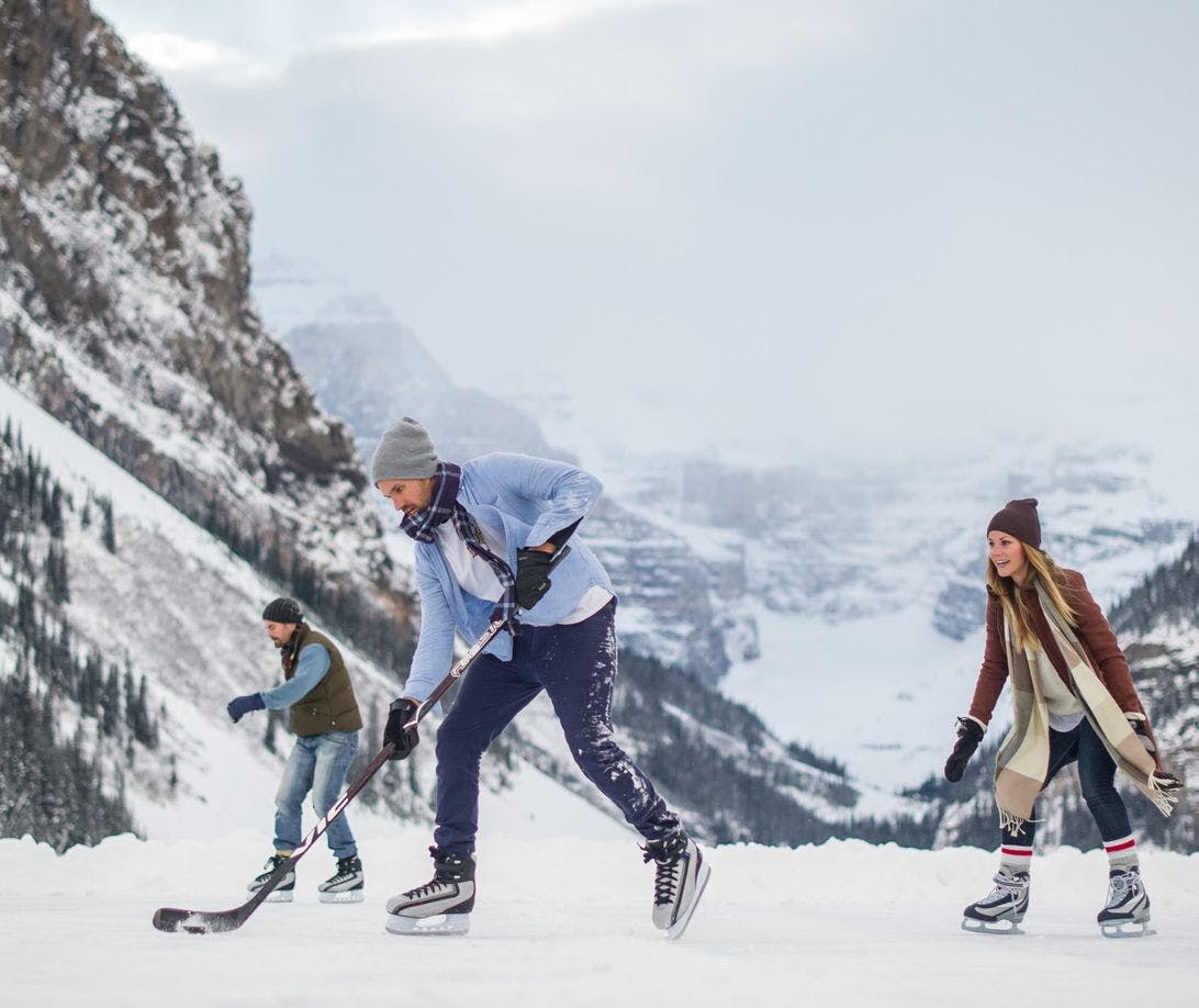 Three friends play hockey on a vast frozen lake with glaciers and mountains in the background