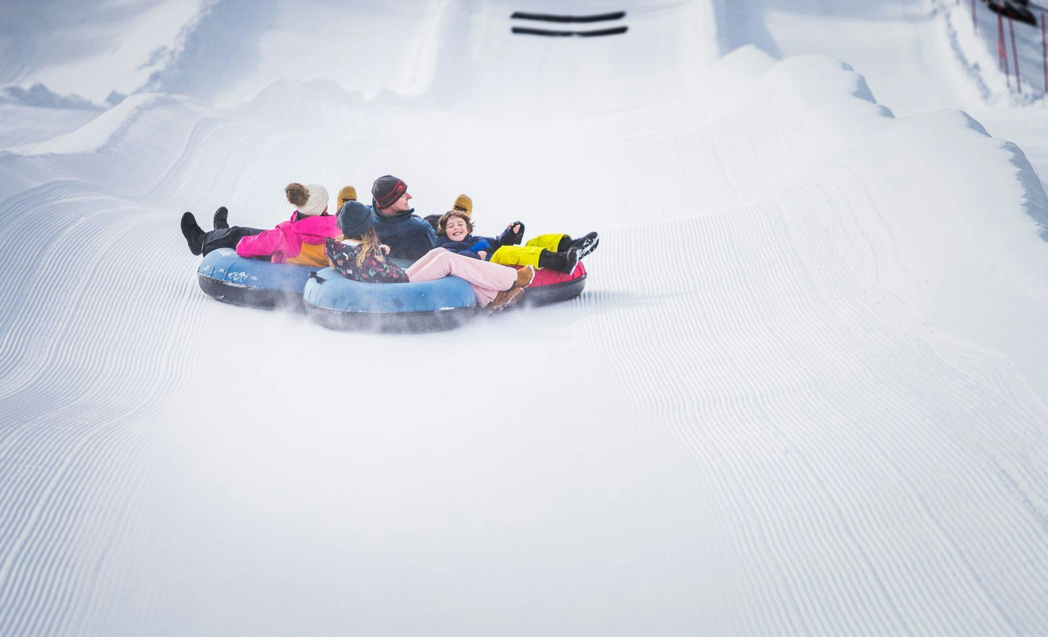 A family of four in separate tubes sliding down a hill together