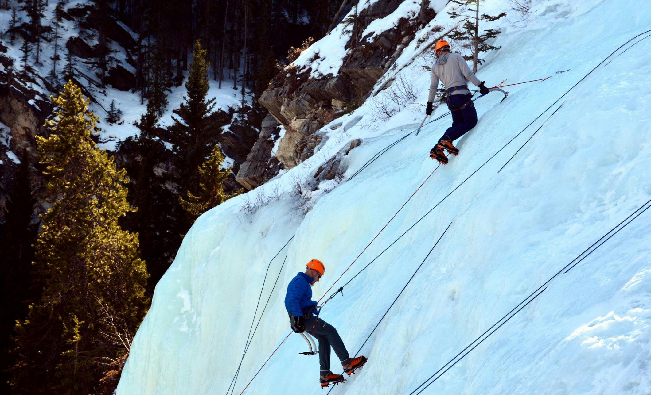 Two ice climbers climbing a frozen waterfall on a sunny winter day