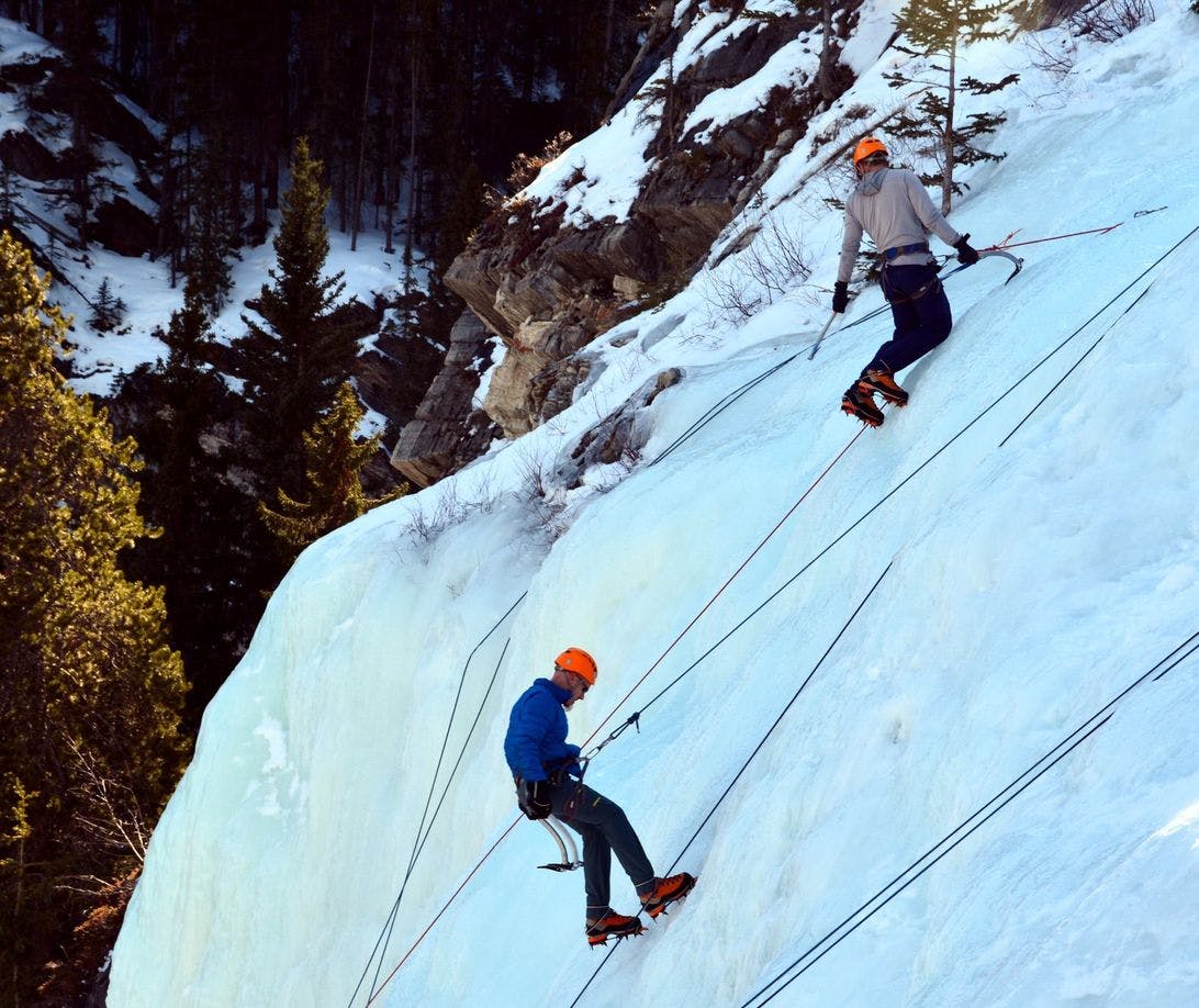 Two ice climbers climbing a frozen waterfall on a sunny winter day