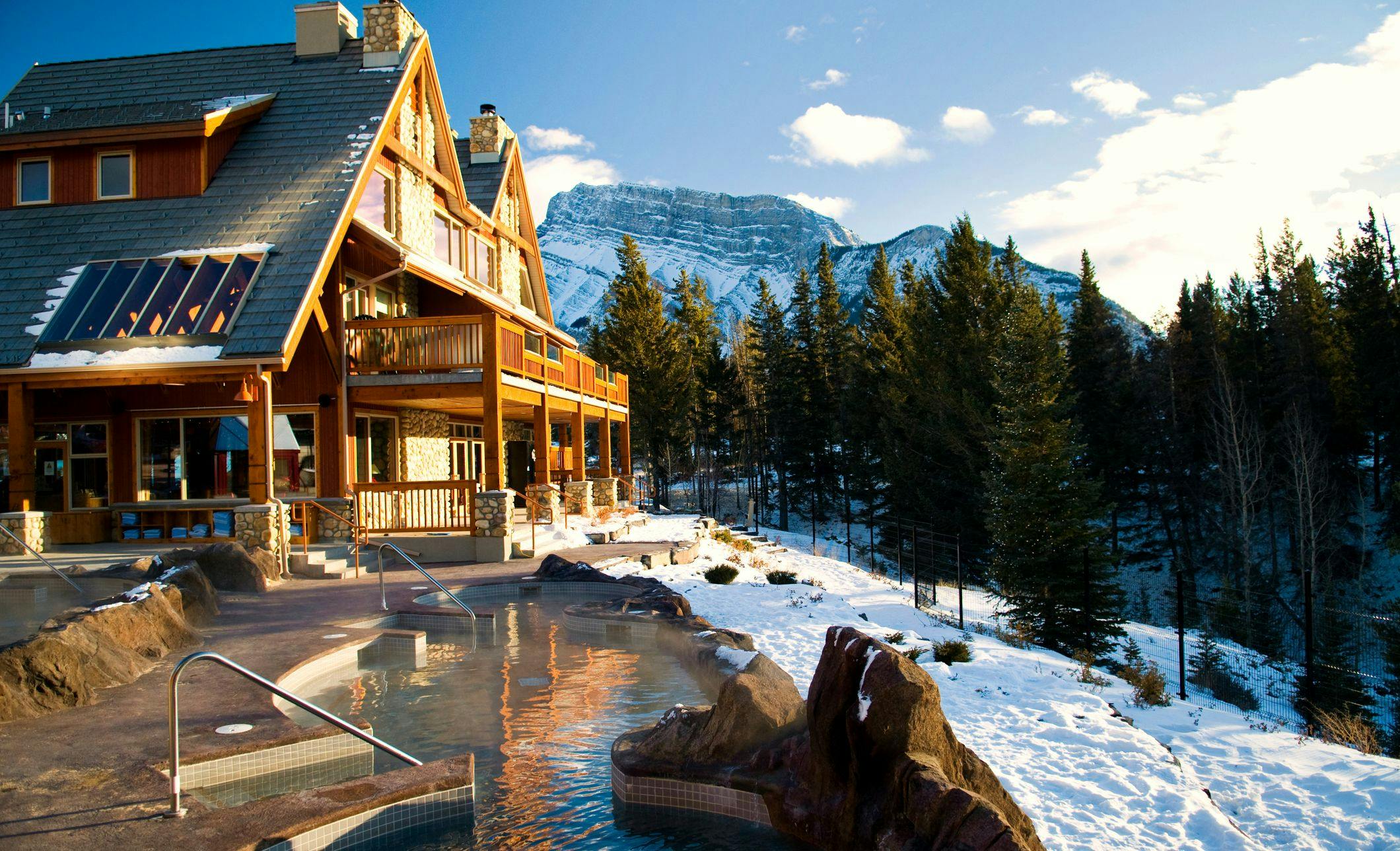 Outdoor Hot Pools with a Wooden Lodge in the Background and Mountains with Snow
