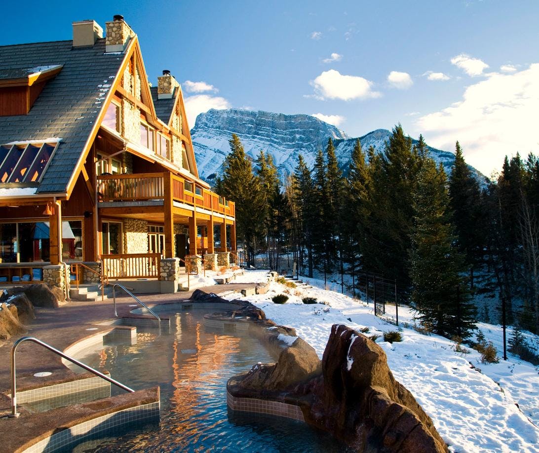 Outdoor Hot Pools with a Wooden Lodge in the Background and Mountains with Snow