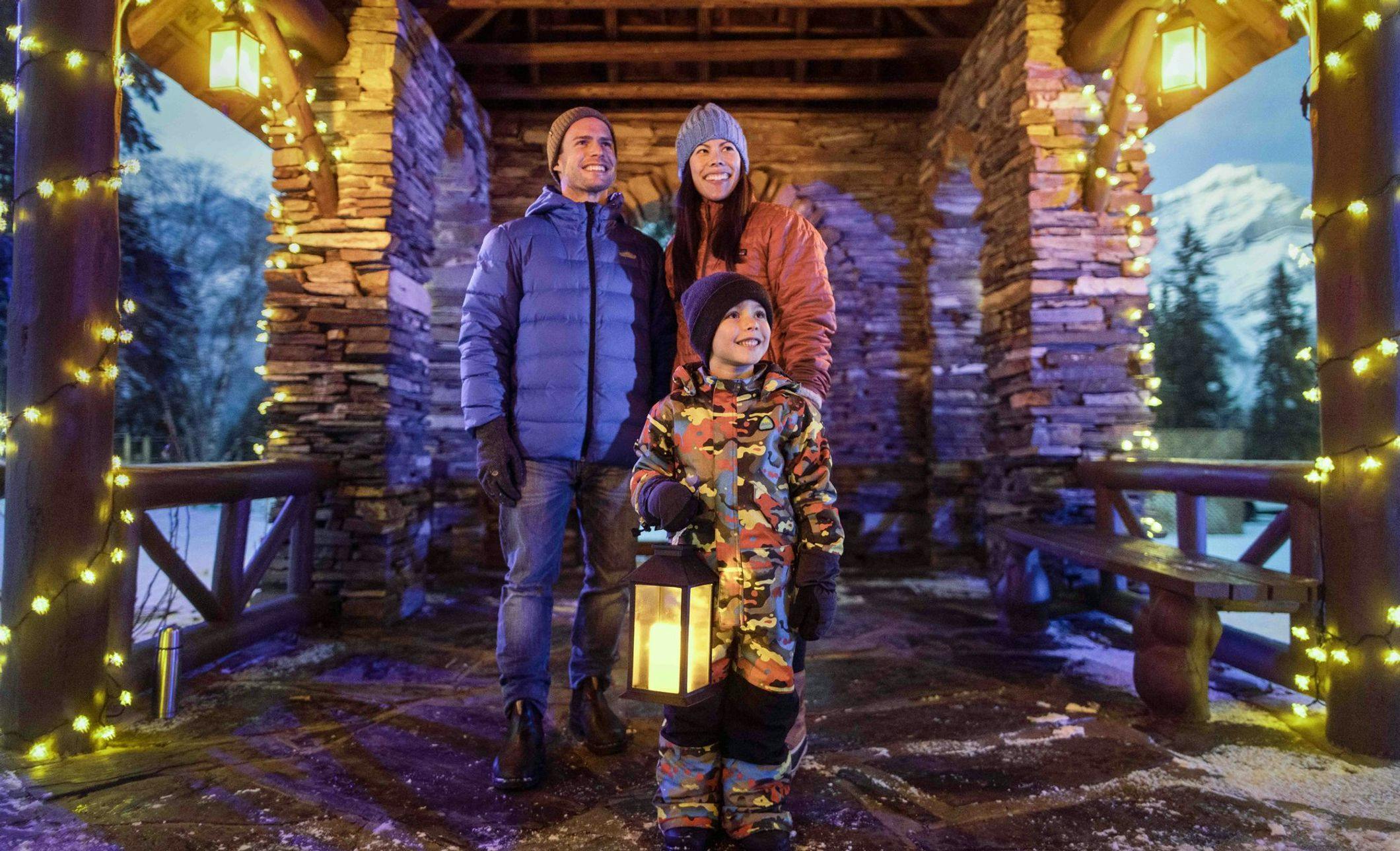 A family exploring Christmas lights using a handheld lantern in the winter months