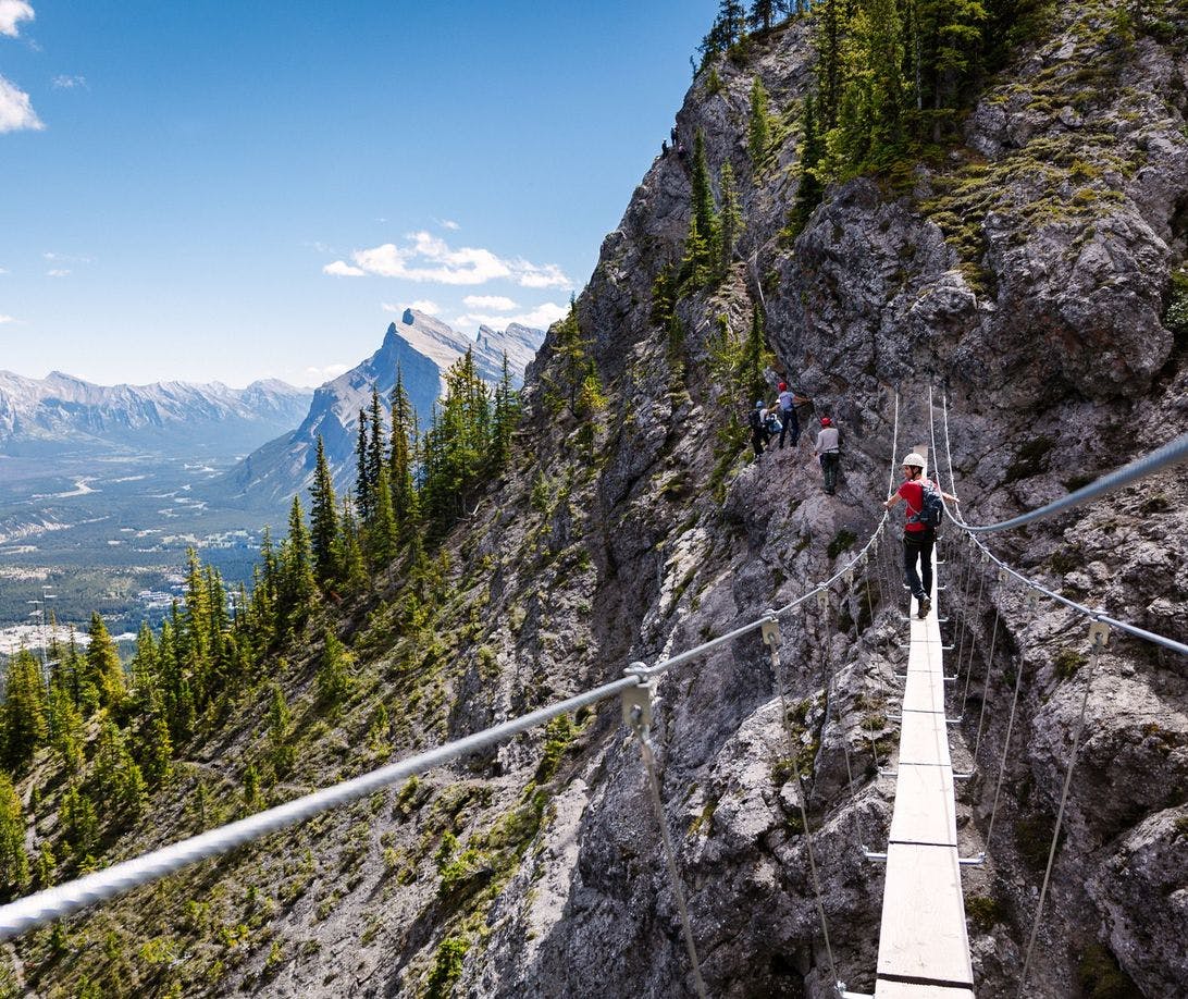 A climber in a harness attached to the cables crosses a bridge high up in the mountains
