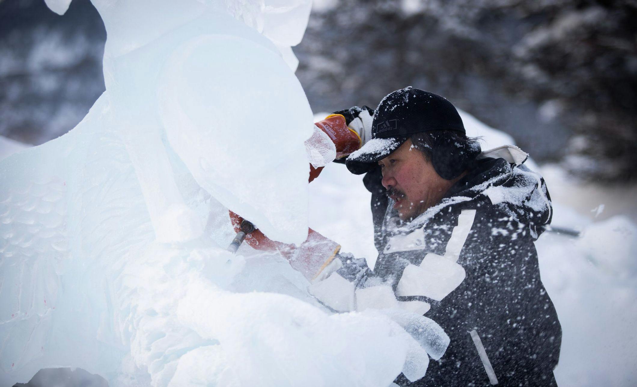 An ice carver using tools to work on a giant ice sculpture