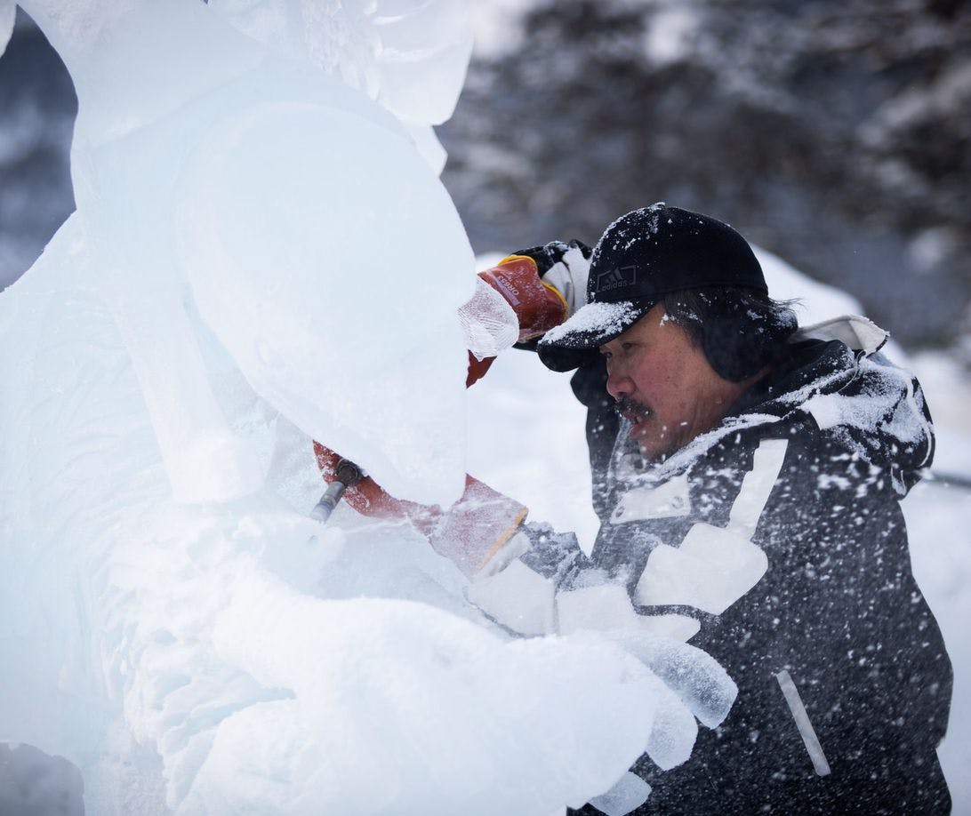An ice carver using tools to work on a giant ice sculpture