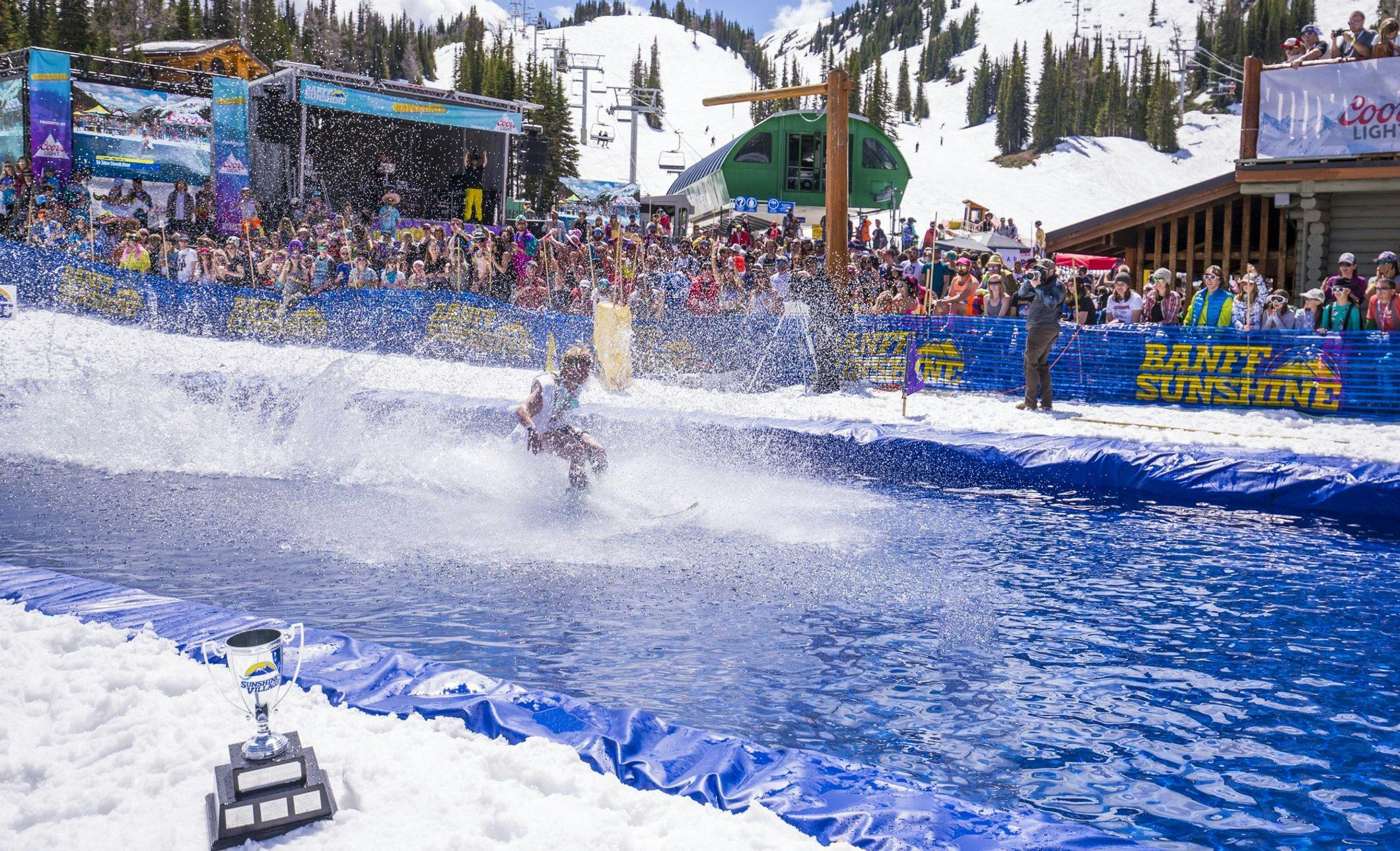A skier tries to glide across water with a large crowd in the background cheering them on during Slush Cup at Banff Sunshine Village in Banff National Park.