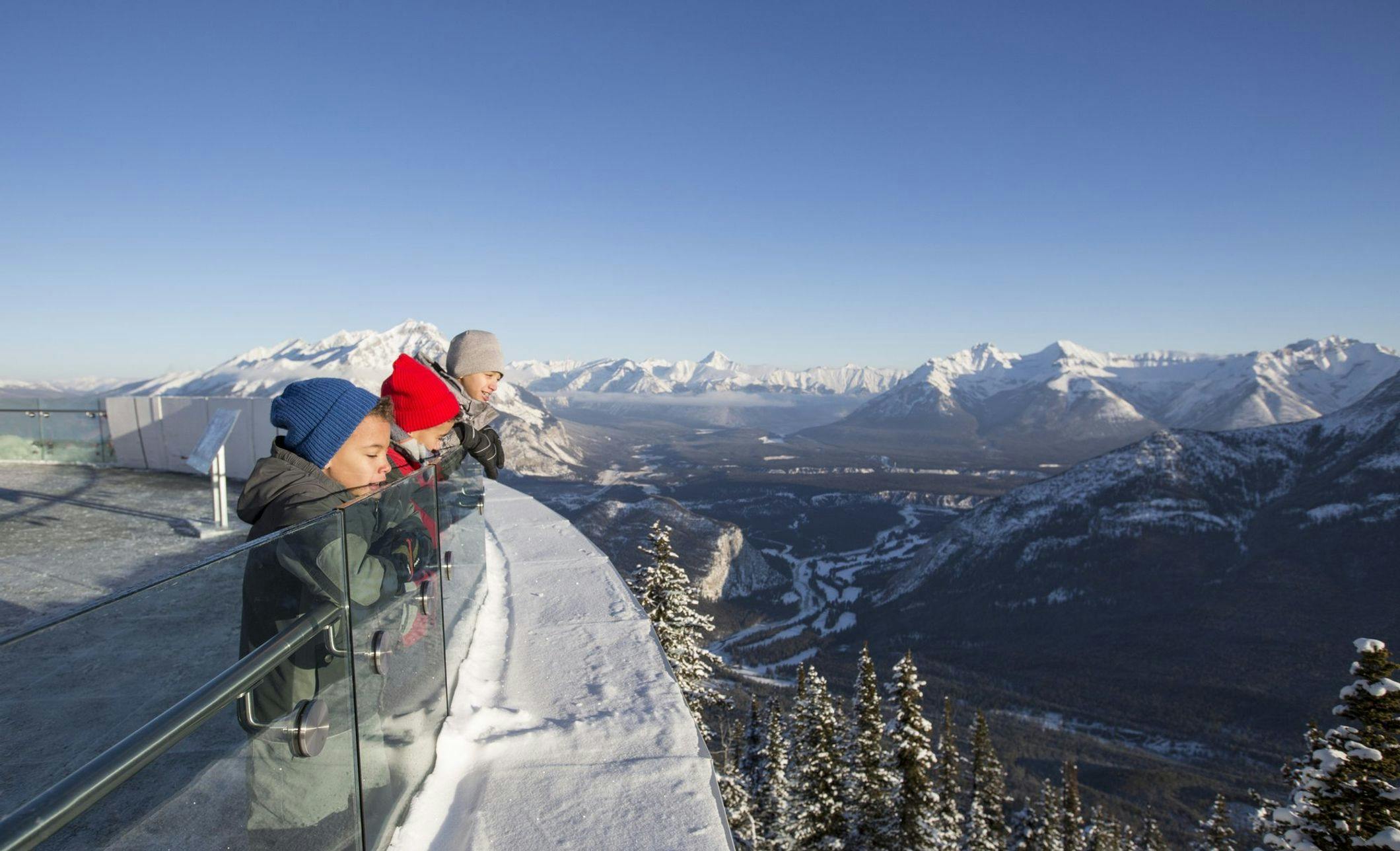Three young boys looking over the viewing platform deck at the Banff Gondola on a snowy winter day