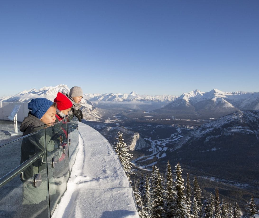 Three young boys looking over the viewing platform deck at the Banff Gondola on a snowy winter day