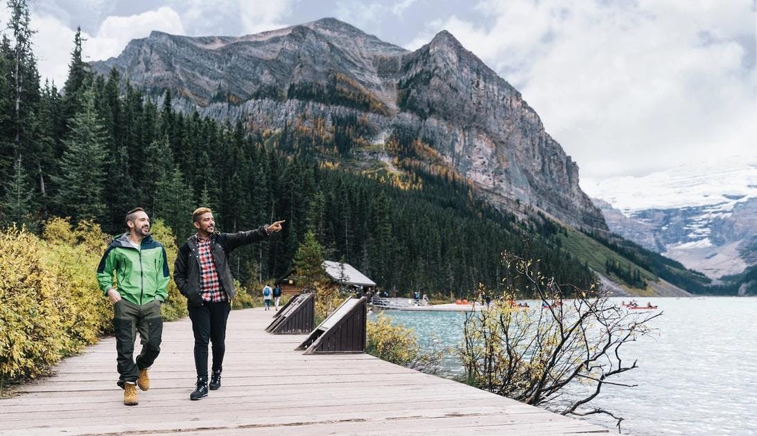 Two men walking along the Lake Louise lakeshore with yellow foliage in the background