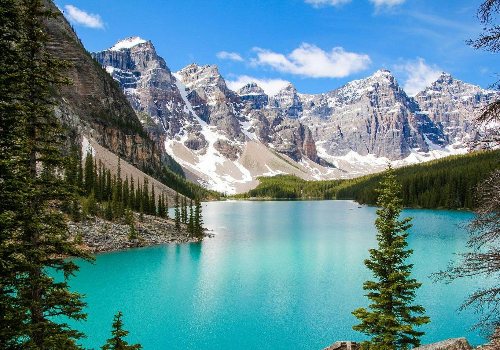 A turquoise lake surrounded by large, snow-capped mountain peaks and tall green trees