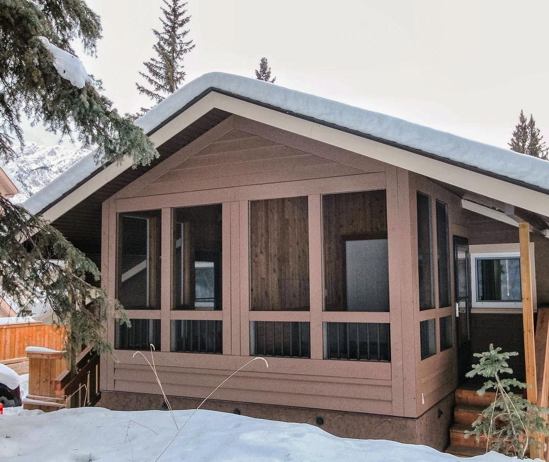 Cabin-style accommodation with a covered front porch, surrounded by snow